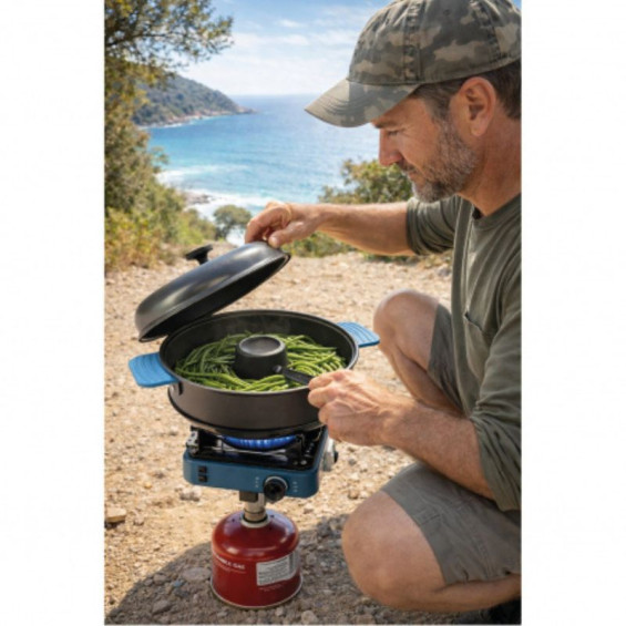 Hombre con ropa de camuflaje y gorra utilizando el horno nómada TANDOOR sobre un hornillo de gas de camping portátil en exterior